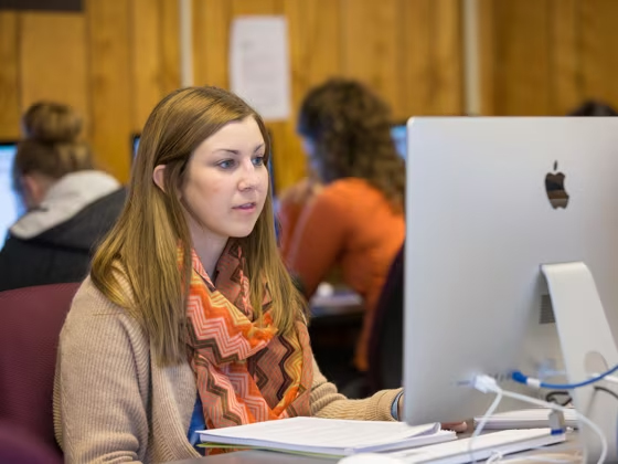Female student sitting and staring at iMac desktop with notebook in front of her