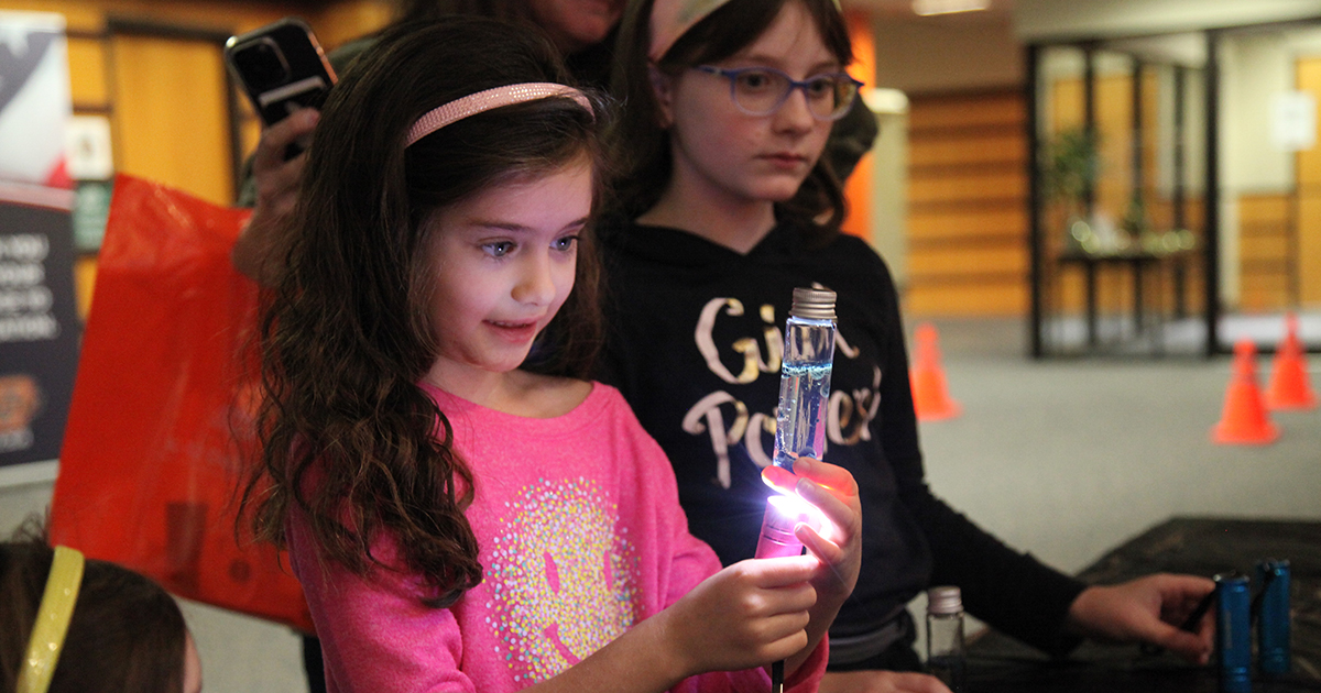 A girl at the 2023 Deck the Halls with STEM event marvels at the glow of her own small lava lamp.