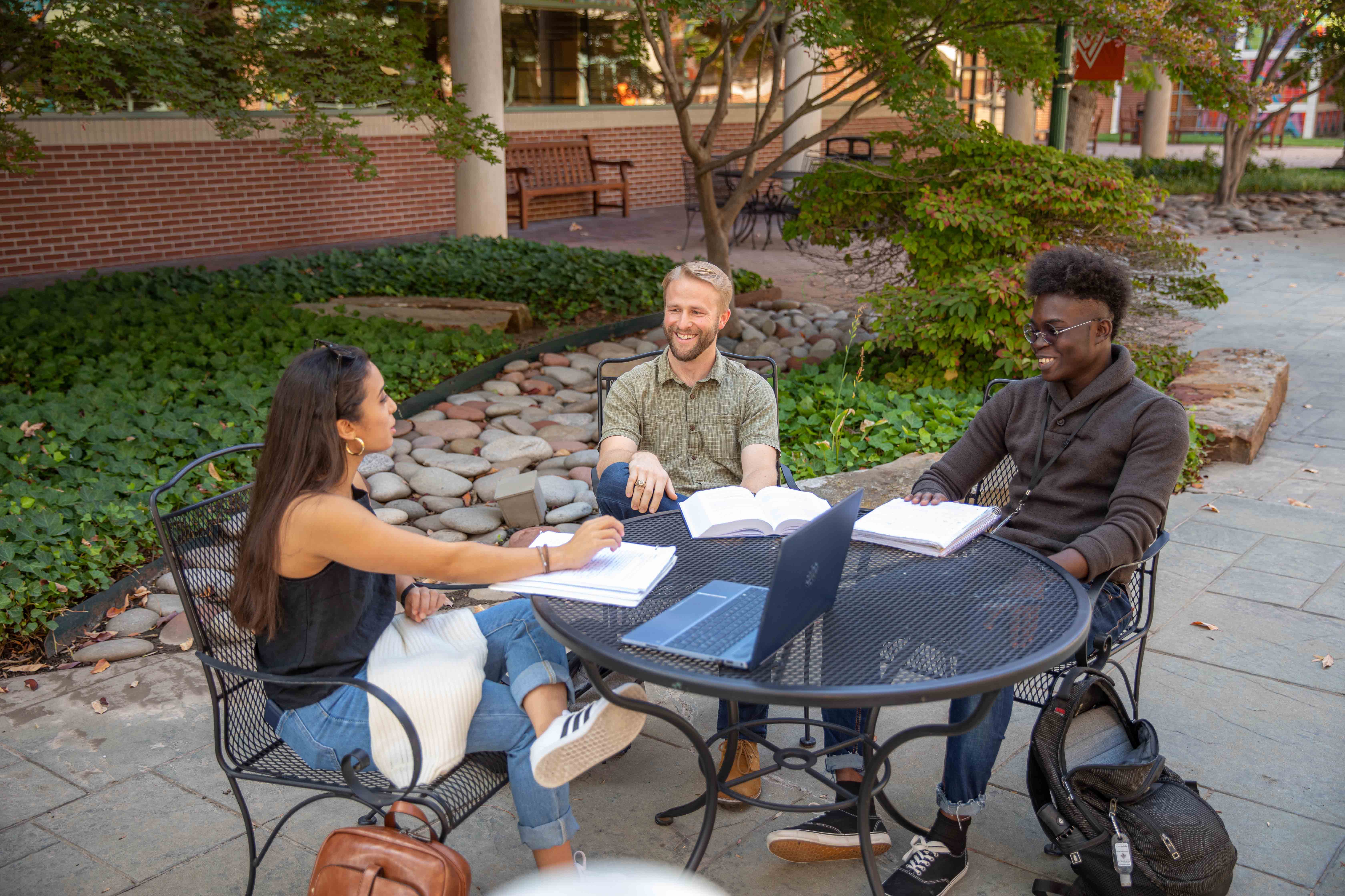 three students sit at courtyard table